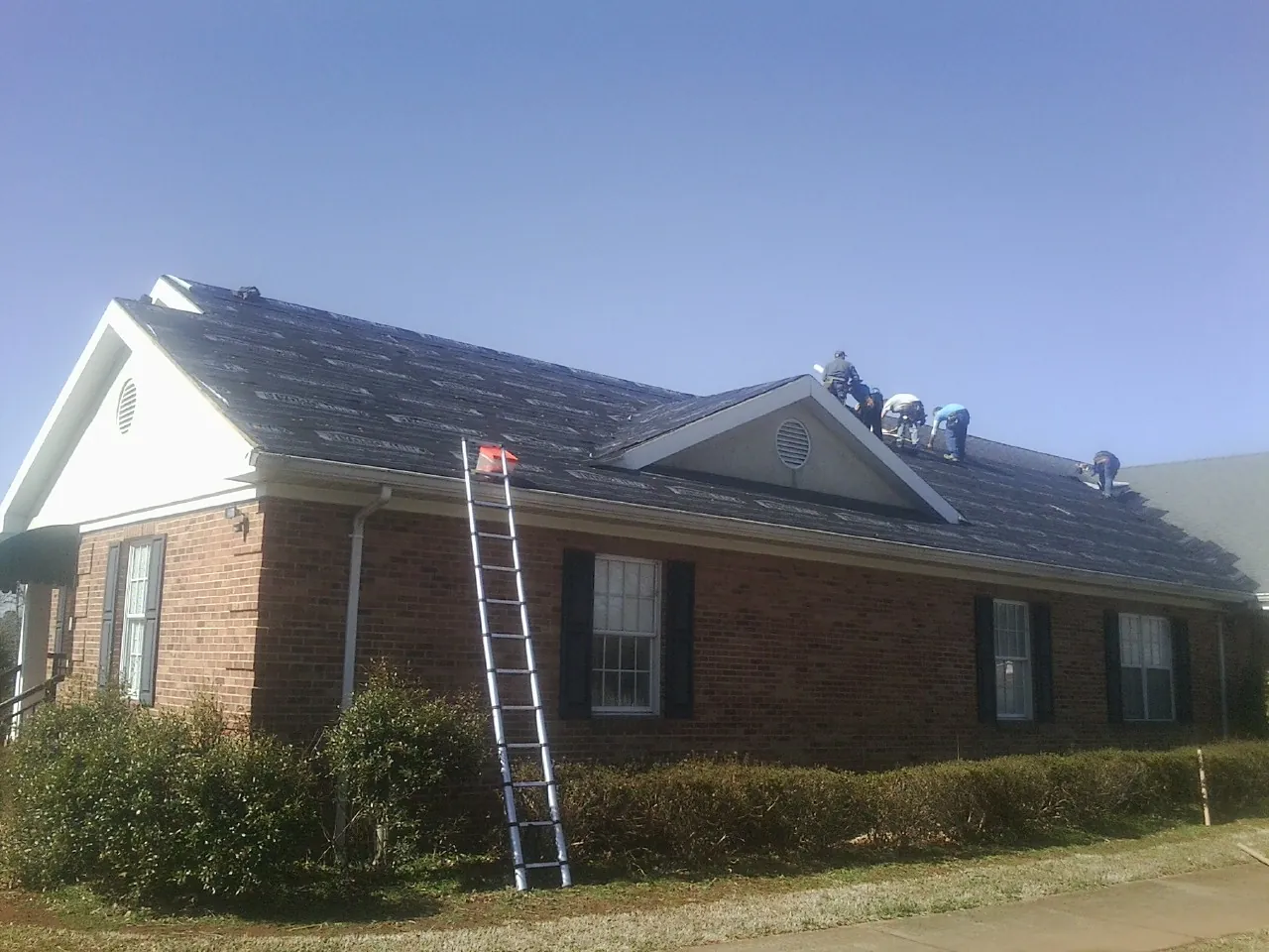 Crew tearing shingles off a brick ranch roof with a ladder set — Metal Roof Repair work by our crew in Cordele