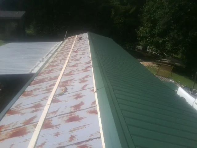 Old rusted panels beside newly installed green metal roofing — Wind Damage Roof Repair by Roofing Brothers in Cordele