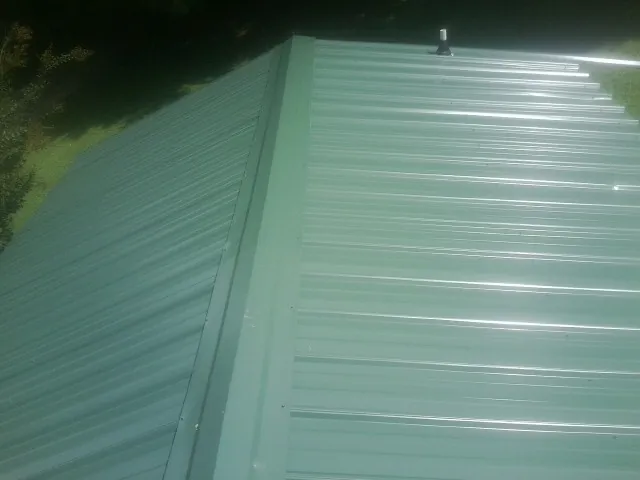 New green metal panels meeting at the ridge of a roof — Flat Roof Repair work by our crew in Cordele