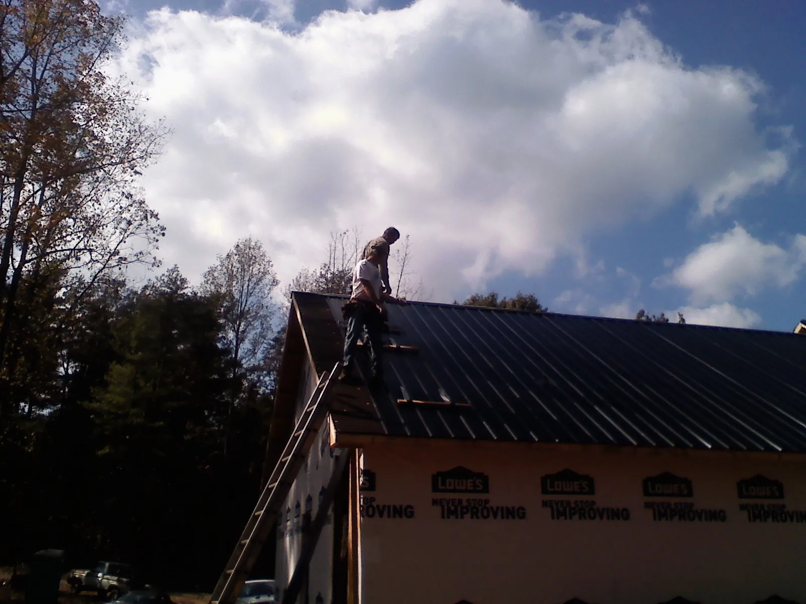 Roofer fastening dark metal panels high against a cloudy sky, from a Roof Inspection job in Cordele