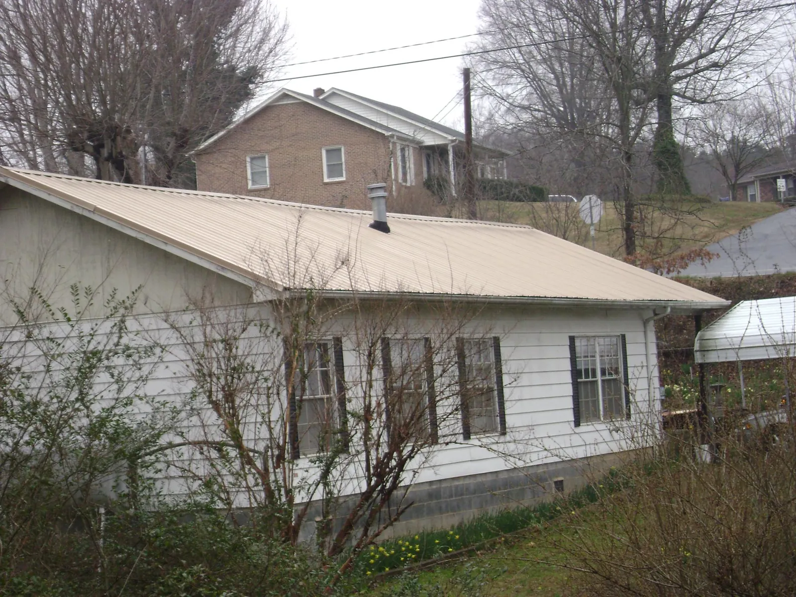 Tan metal roof on a white sided house set into a hillside — Commercial Roofing by Roofing Brothers in Cordele