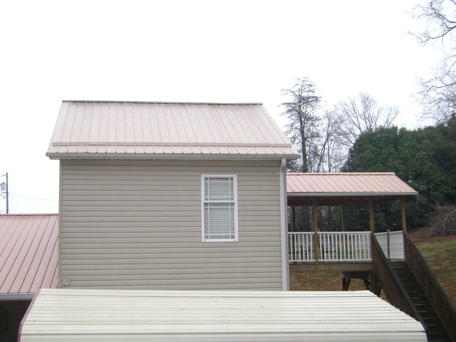 Tan metal roofs on a two story addition and attached porch, from a Roof Replacement job in Cordele